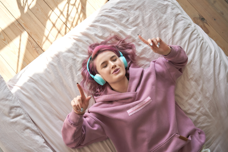 Conditions location loi Pinel – Une jeune fille allongée sur sont lit en écoutant de la musique