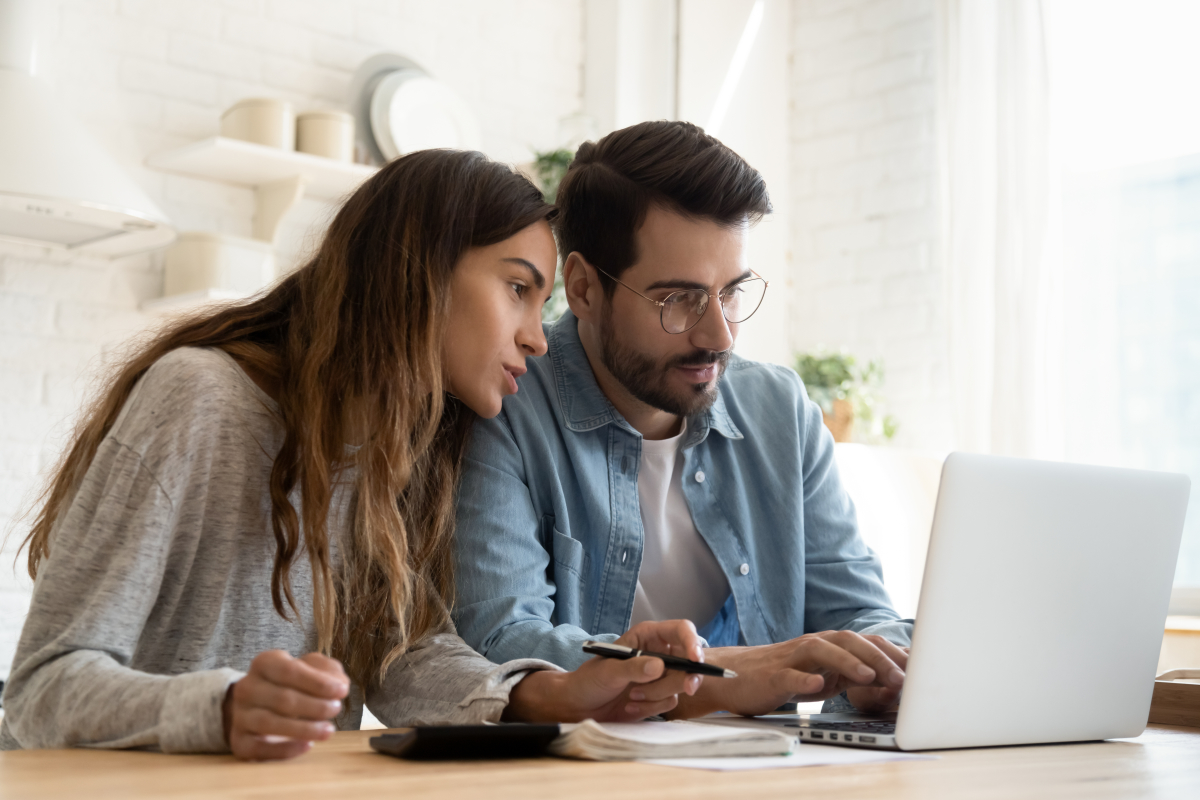 Premier investissement locatif – Jeune couple en train de faire de recherche sur un ordinateur en prenant des notes 