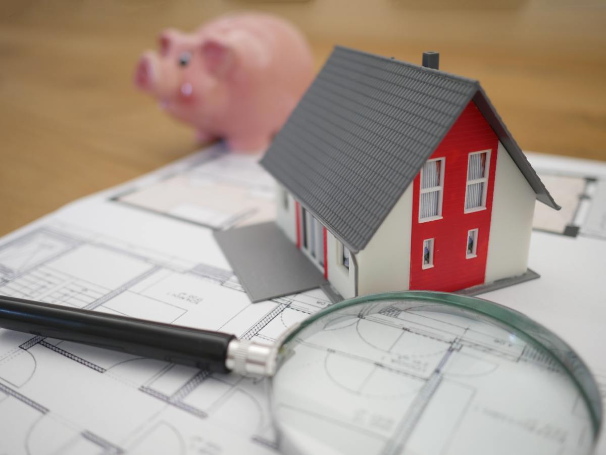tendances du marché immobilier 2022 – une maison miniature sur un plan d’un logement avec une loupe et un cochon tirelire