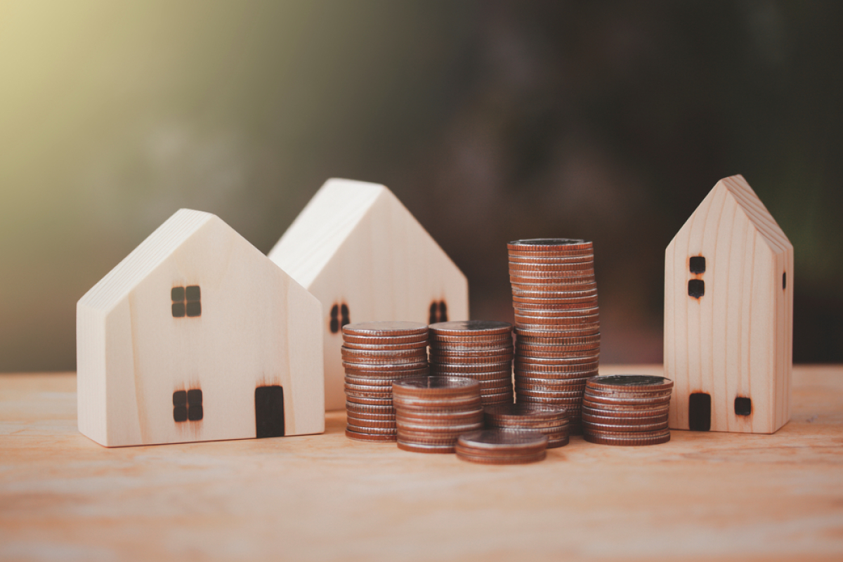 investisseur immobilier – Des maisons miniatures en bois avec des piles de pièces montrant la croissance d’un investissement immobilier