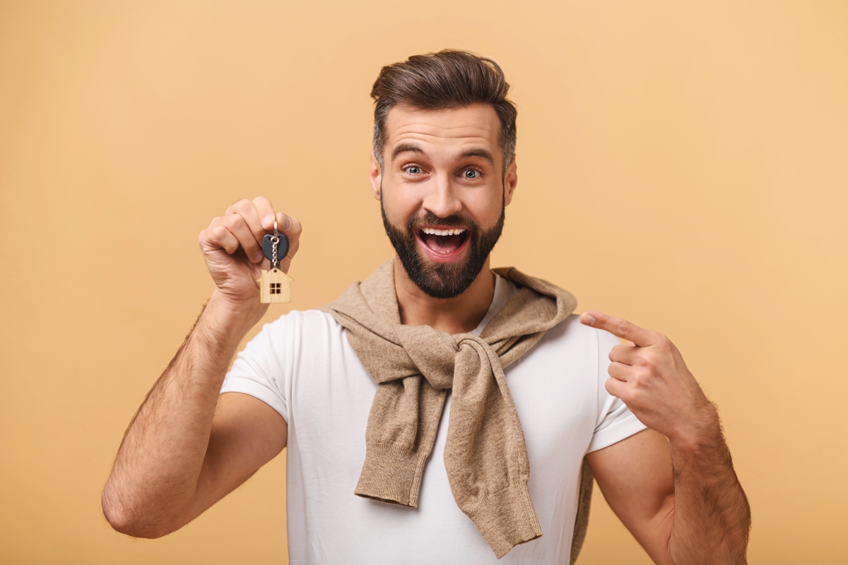 un homme avec un pull beige noué sur les épaules, souriant avec un trousseau de clés