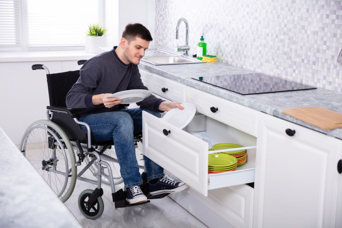 Normes PMR logement neuf — Une personne en situation de handicap en train de ranger de la vaisselle dans sa cuisine
